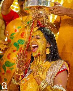 a woman is covered in yellow powder and throwing water on her head as she smiles