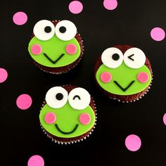 three cupcakes with green icing and pink polka dots on a black surface