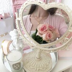 a woman is looking at her reflection in a mirror with pink roses on the table