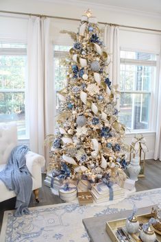 a white christmas tree with blue and gold ornaments in a living room setting, surrounded by windows