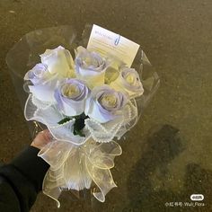 a person holding a bouquet of white roses in their hand with a note on it