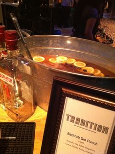 a table topped with a metal bowl filled with liquid and lemons next to a framed sign