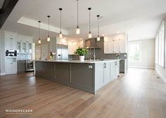 a large kitchen with white cabinets and wood flooring is pictured in this image, there are lights hanging from the ceiling