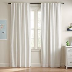 a white curtain hanging on the side of a window next to a dresser with drawers