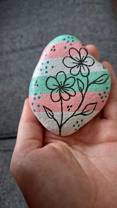 a hand holding a painted rock in the shape of a heart with flowers on it