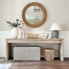 a table with a mirror, lamp and vase on it in front of a white wall