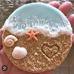 a hand holding a cookie decorated with sea shells and starfish on the top, along with a heart in the middle