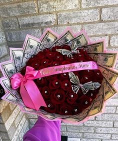 a woman holding a bouquet of roses with money in the back and pink ribbon around it