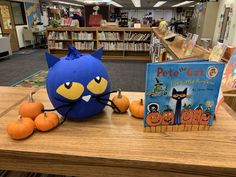 a blue cat stuffed animal sitting on top of a table next to two pumpkins