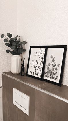 two framed pictures sitting on top of a wooden cabinet next to a vase with flowers