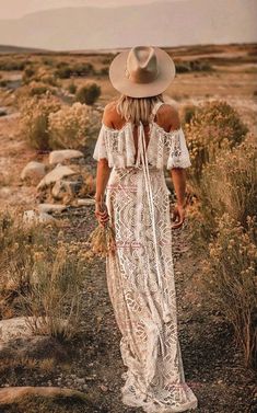 a woman in a white dress and hat walks through the desert with her back to the camera