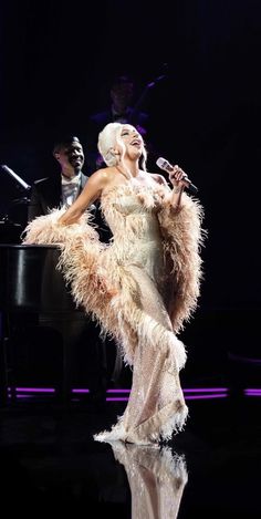 lady in feathery dress standing next to a grand piano and singing into a microphone