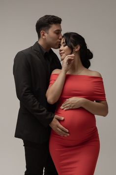 a pregnant woman in a red dress is standing next to a man wearing a black suit