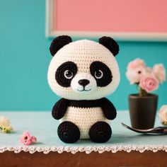 a crocheted panda bear sitting on top of a table next to a flower pot