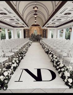 an indoor wedding venue with white chairs and flowers on the aisle, decorated with monogrammed letters