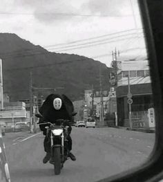 a black and white photo of a person on a motorcycle driving down the street in front of some buildings