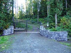 a gated driveway leading into a wooded area with stone walls and gates on either side