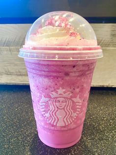 a pink starbucks drink with whipped cream and sprinkles on the top is sitting on a table