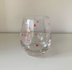 a clear glass with hearts on it sitting on a table next to a white wall