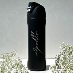 a black water bottle sitting next to some white flowers