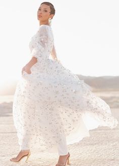 a woman in a white dress and heels is standing on the sand with her arms behind her back