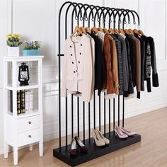 a rack with shoes and coats hanging on it in front of a white wall next to a shelf