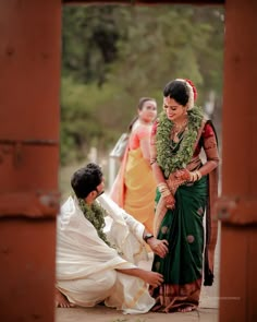 a man kneeling down next to a woman in a green sari and white outfit