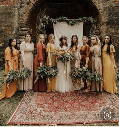 a group of women standing next to each other in front of a wedding arch with greenery