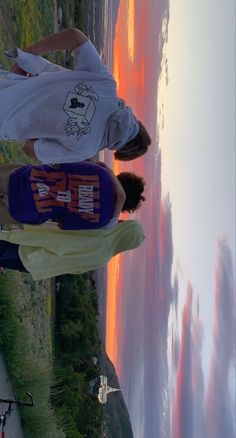 two young men standing next to each other on top of a cliff near the ocean