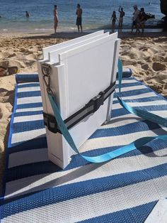 an ice chest sitting on top of a blue and white striped blanket next to the ocean