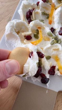 a person holding a cookie with fruit and cream toppings on it in front of a white plate