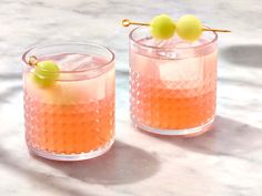 two glasses filled with drinks sitting on top of a marble counter next to each other