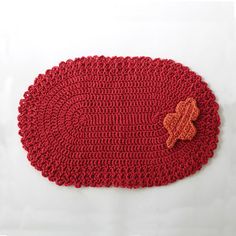 a red crocheted placemat with an orange flower on the center and a brown button in the middle