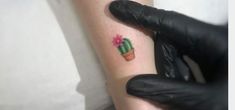 a small cactus tattoo on the left inner arm, with pink flowers and green leaves