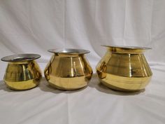 three shiny gold vases sitting on top of a white tablecloth covered floor next to each other