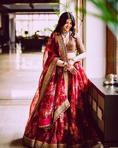 a woman in a red and gold bridal gown posing for the camera with her hands on her hips