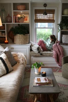 a woman sitting on a couch in front of a window next to a coffee table