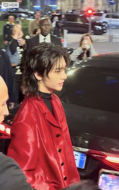 a woman in a red coat is standing next to a black car and some people