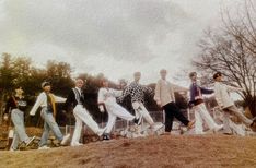 a group of young men standing on top of a grass covered hill next to trees