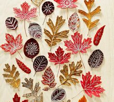 a bunch of different colored leaves on a white table cloth with gold and silver foil