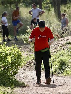 a man walking with crutches on a trail in the woods while other people are running behind him