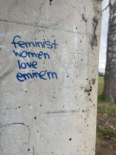 graffiti written on the side of a cement pillar in front of some trees and grass