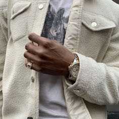 a man in a white jacket is holding his hand on his wrist and wearing two gold rings