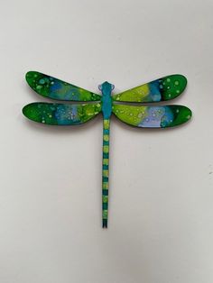 a green and blue dragonfly sitting on top of a white surface