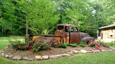 an old rusted truck is sitting in the middle of a flower bed with pink flowers