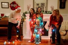 a group of people standing in front of a fire place with christmas lights on them