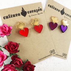 two heart shaped earrings sitting on top of a piece of paper next to red roses