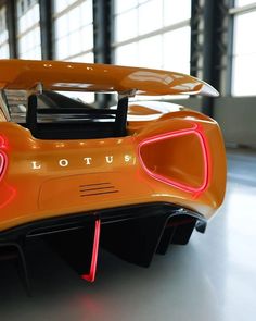 an orange sports car with its hood up and lights on, parked in a garage