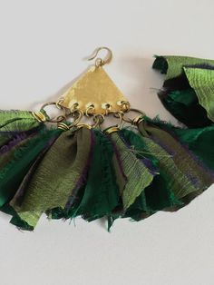 a green and purple necklace with gold bells on it's end, hanging from a hook