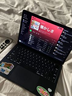 an open laptop computer sitting on top of a bed next to a cell phone and remote control